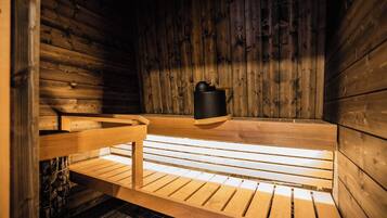 Una sauna con paredes y bancos de madera, un calentador negro y suelo de piedra.