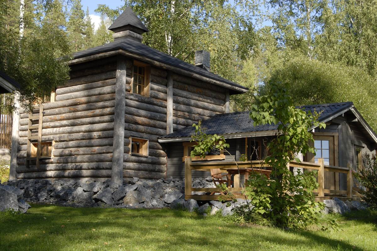 Eine Blockhütte mit Stein Fundament, Holzterrasse und Schornstein.