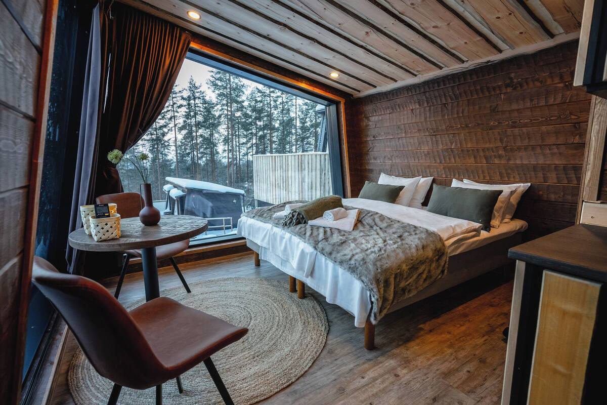 Ein gemütliches Schlafzimmer mit einem Bett, einem kleinen Tisch und einem Sessel. Ein Fenster bietet Blick auf Bäume.