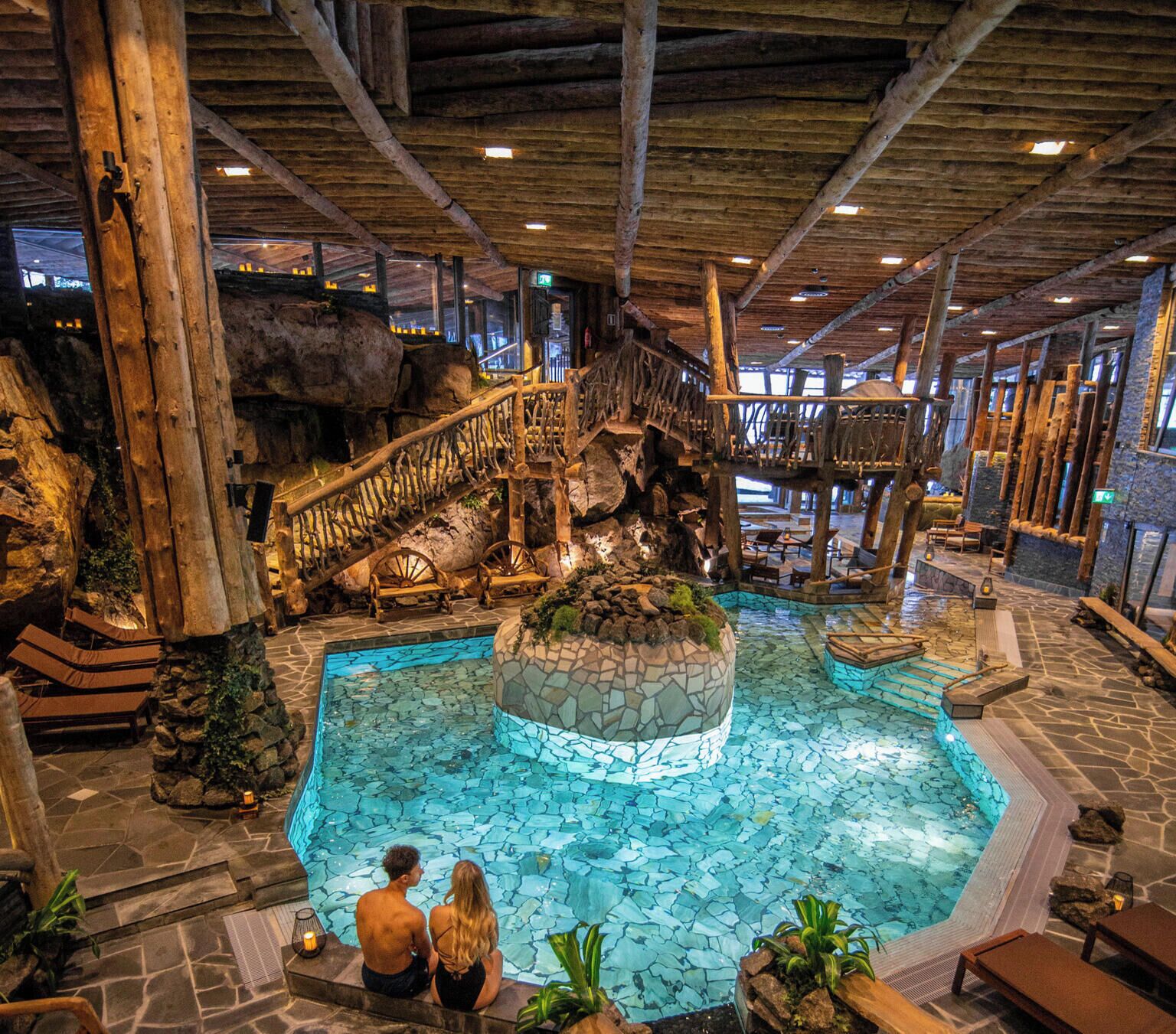 Une piscine intérieure dotée d’un îlot central, de poutres en bois et d’un revêtement de sol en pierre.