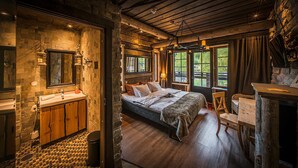 A rustic bedroom with a stone wall, wooden bed, and a view of greenery outside.