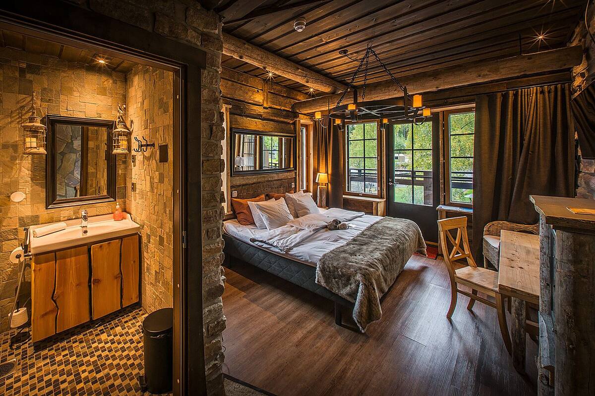 Ein rustikales Schlafzimmer mit Steinwand, Holzbett und Blick auf Grün.
