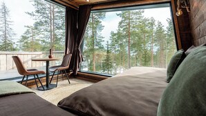 A bedroom with a large bed, a small table, two chairs, and a view of trees through a large window.