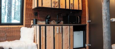 El interior de una cabaña con un armario de madera, un sillón blanco y mullido, un microondas y un refrigerador pequeño.