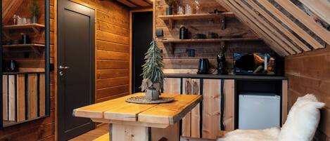 A cozy cabin with a wooden interior, a small kitchen area, and a white furry chair.