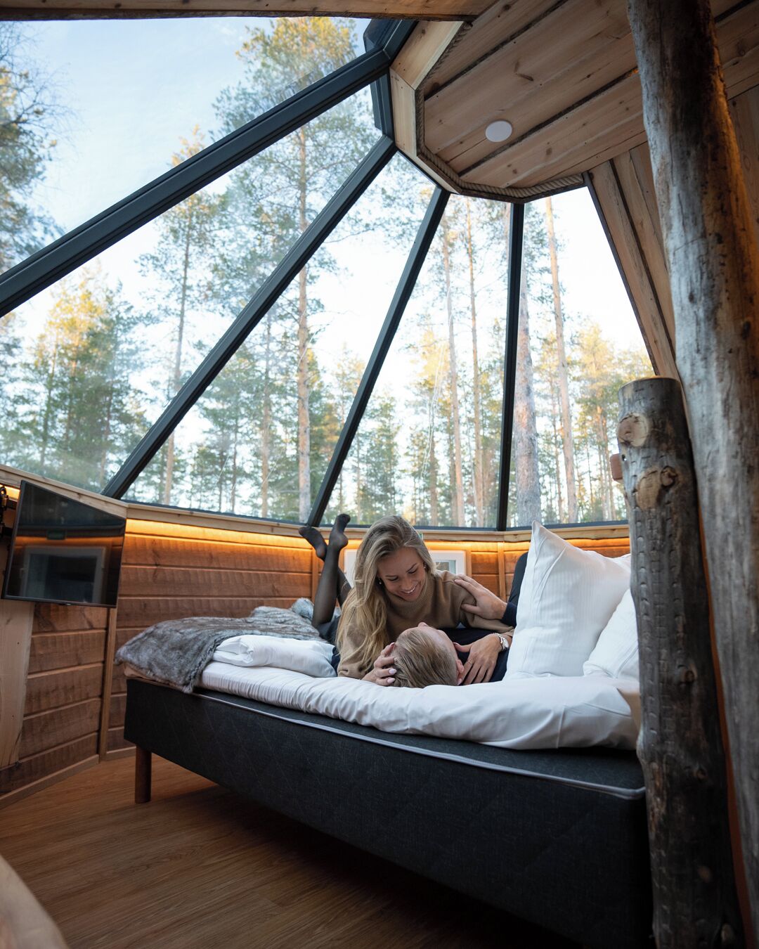 Une cabane chaleureuse avec une grande lucarne, des murs en bois et un lit avec des oreillers.