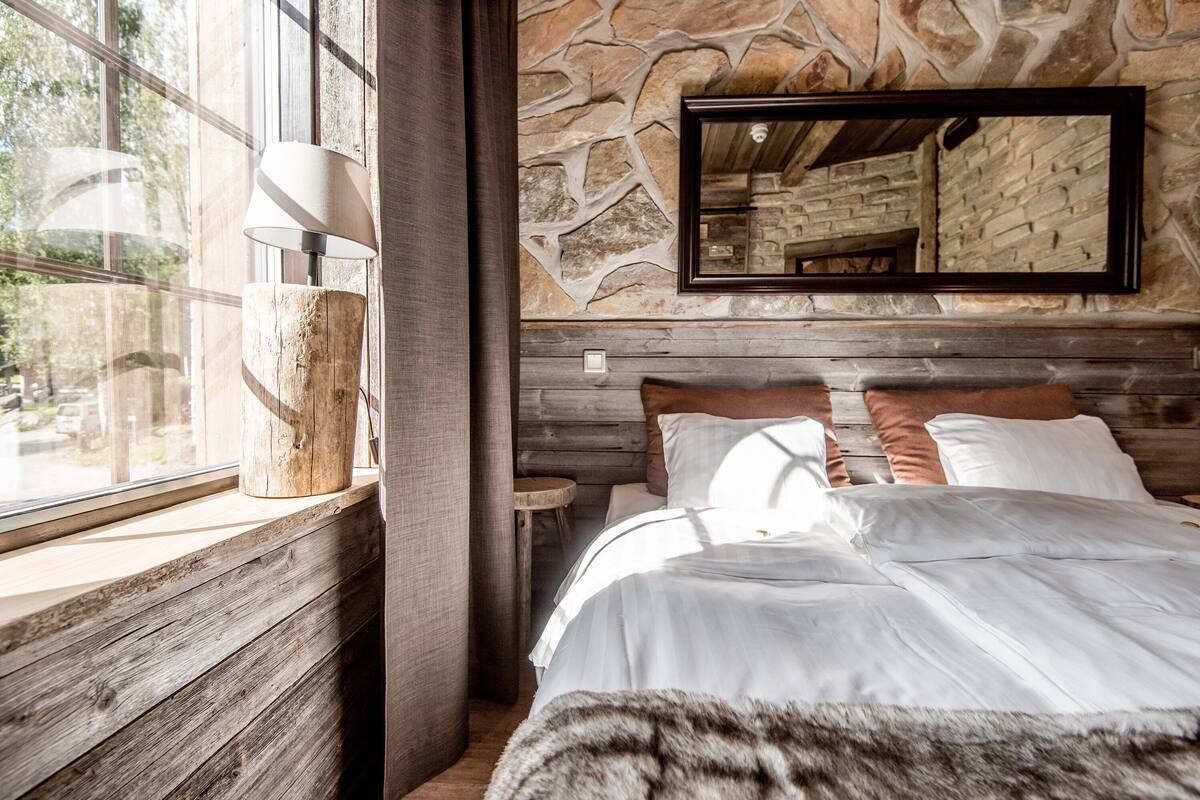 Ein Schlafzimmer mit einer Steinsäule, einem Holz-Kopfteil, einem großen Spiegel und einem Fenster mit Blick ins Freie.