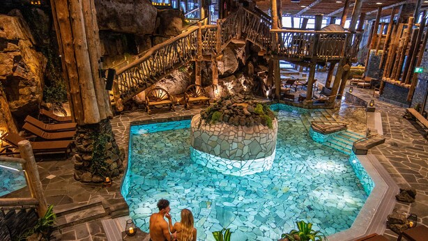 An indoor pool with a wooden deck and a stone fountain.