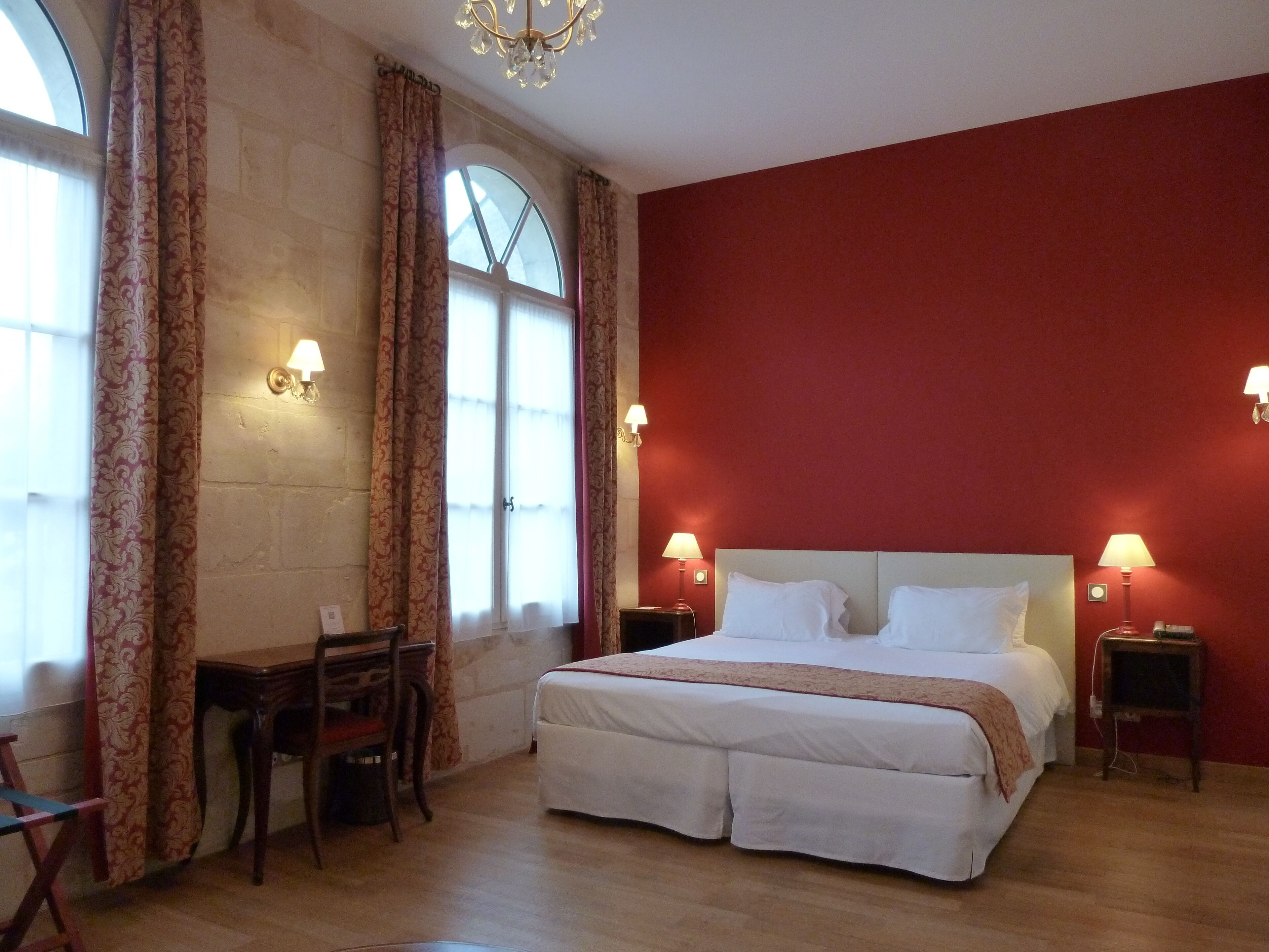 A hotel room with a large bed, two bedside tables with lamps, a desk with a chair, and a window with curtains.