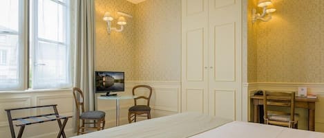 A hotel room with a bed, two chairs, a small table, a television, and a fireplace.