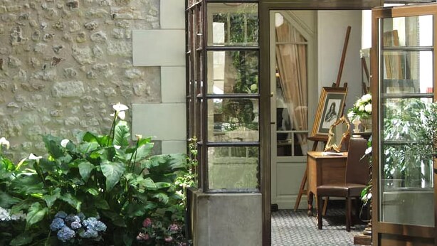 A room with a stone wall, a wooden easel with a painting, and a potted plant.