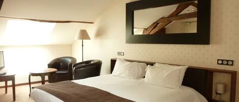 A hotel room with a large bed, a desk with a chair, a lamp, and a mirror on the wall.