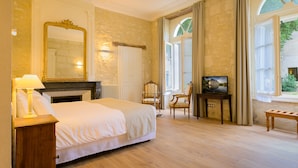 A hotel room with a large bed, a fireplace, a mirror, and a television on a small table.