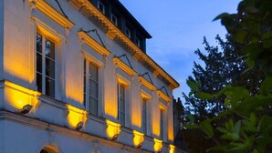 A classical building with symmetrical architecture, large windows, and a well-maintained garden area.