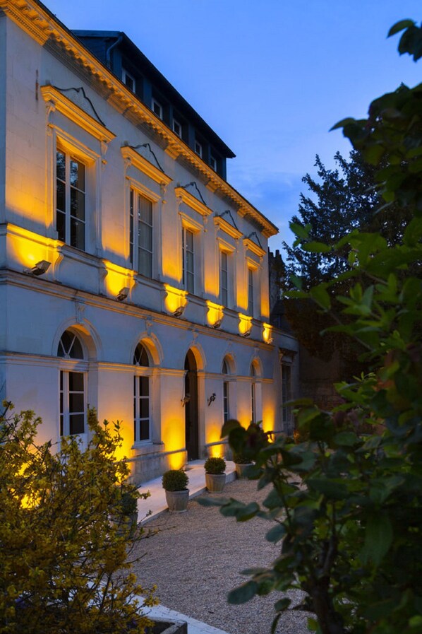 A classical building with symmetrical architecture, large windows, and a well-maintained garden area.