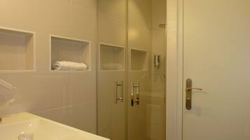 A bathroom with a white sink, a glass shower enclosure, and two towel shelves.