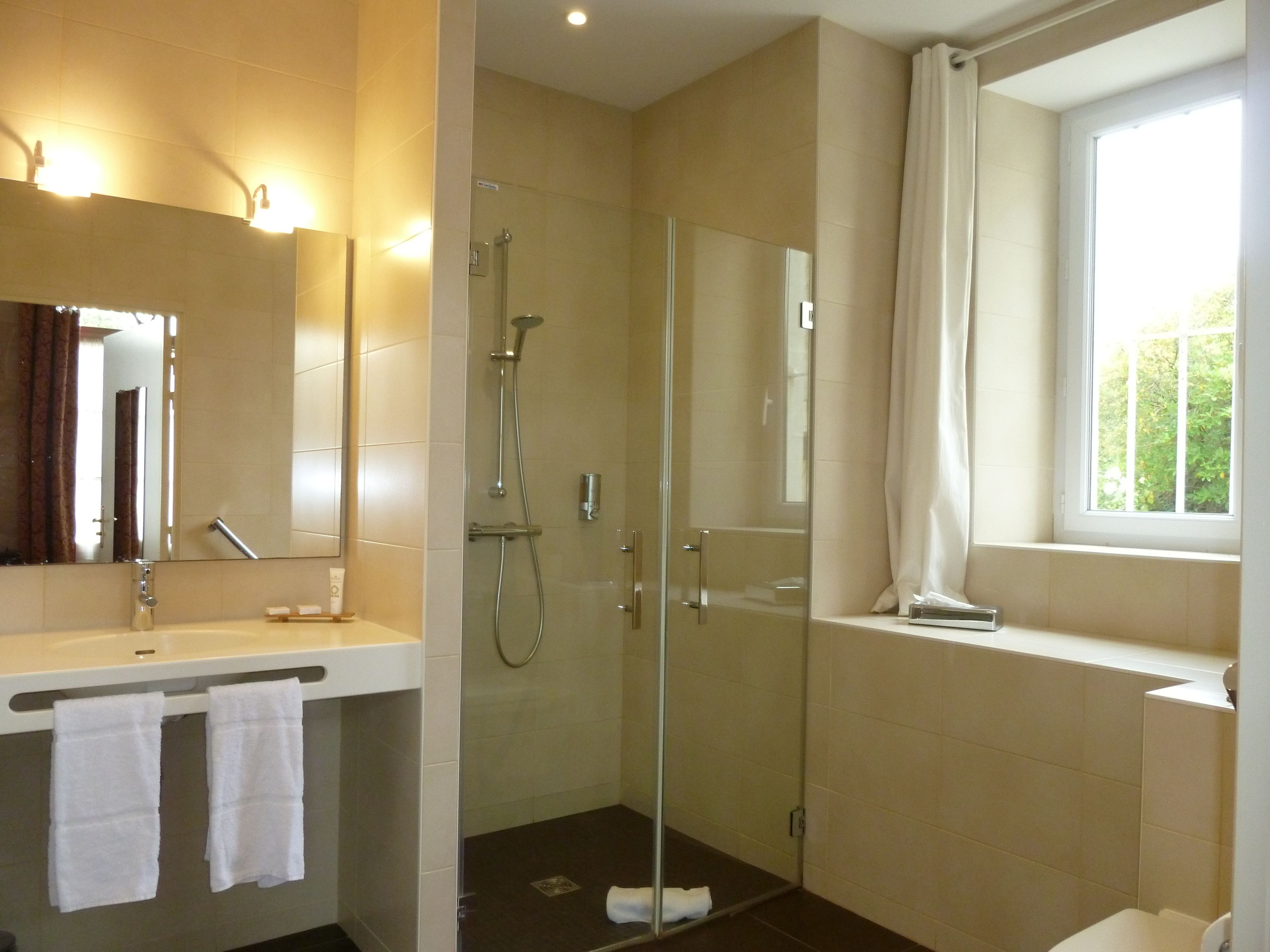 A modern bathroom with a glass-enclosed shower, a vanity with a mirror, and a window providing natural light.
