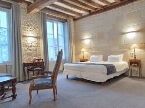 A bedroom with a large bed, two bedside lamps, a stone wall, and a wooden chair.