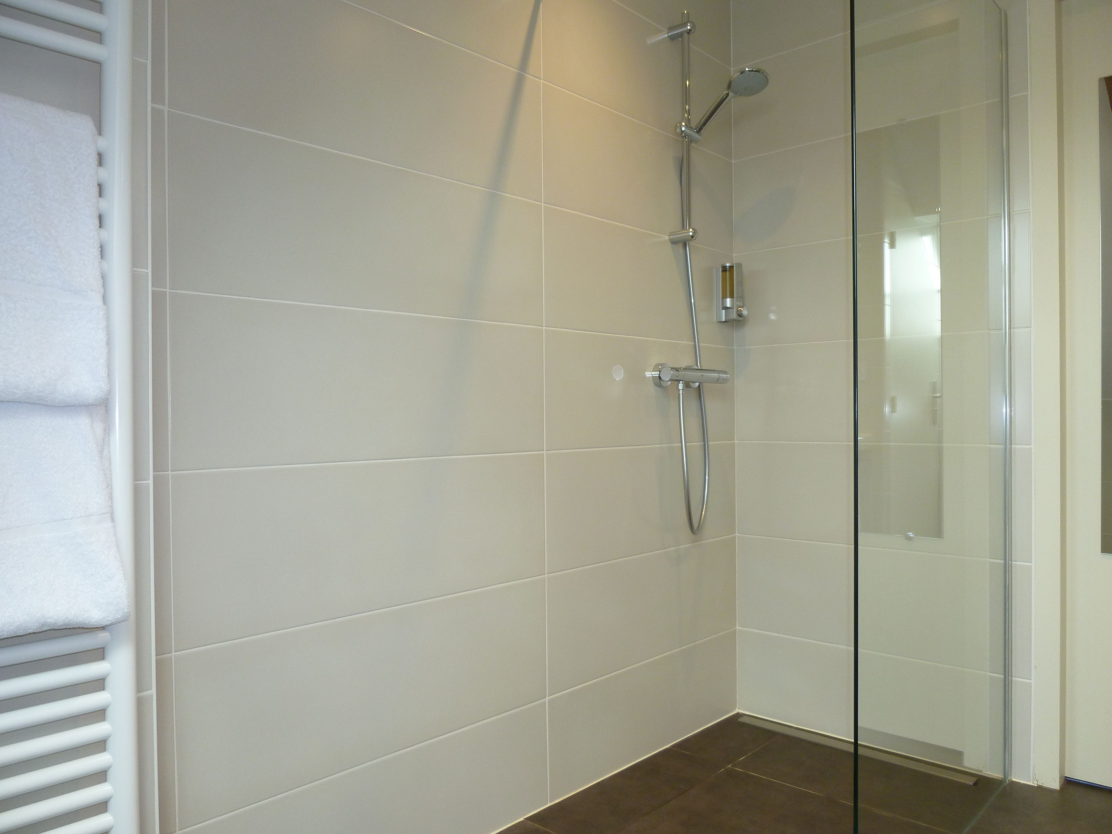 A modern bathroom with white tiles, a glass shower enclosure, and a towel rack.