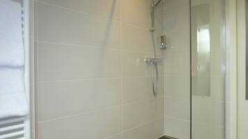 A modern bathroom with white tiles, a glass shower enclosure, and a towel rack.