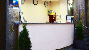 Zona de recepción de un hotel con pared de piedra, un mostrador de recepción, un reloj y una planta pequeña.