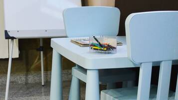 Una sala de reuniones pequeña con una pizarra, dos sillas azul claro y una mesa con un cuaderno y un portalápices.