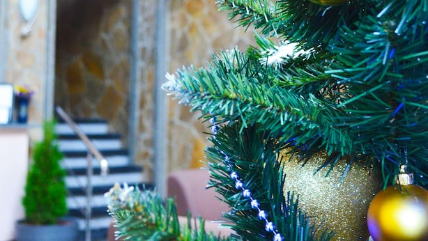Un árbol de Navidad con adornos dorados y azules, situado en el vestíbulo de un hotel con una escalera y una pared de piedra al fondo.