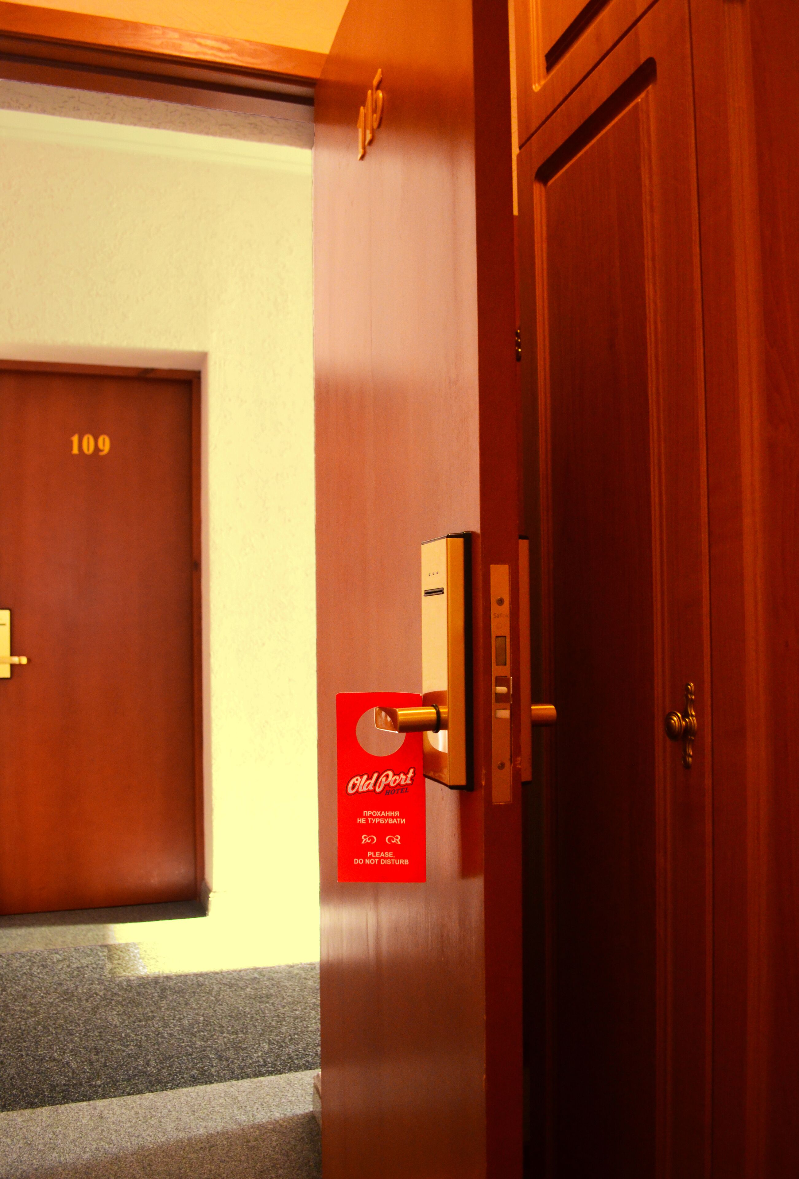 Une chambre d’hôtel avec une porte en bois, un panneau rouge sur le mur et un interphone.
