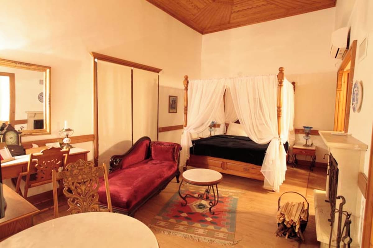 Un dormitorio con una cama con dosel, un sofá rojo, una mesa redonda y techo de madera.