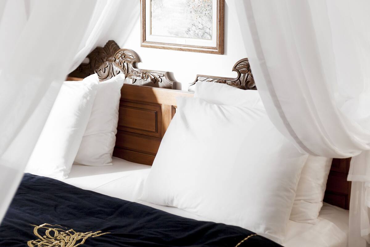 A bed with white linens, a dark blue bedspread with a gold design, and a wooden headboard.