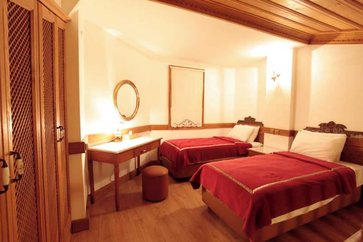 A hotel room with two beds, a desk, a mirror, and a wooden wardrobe.