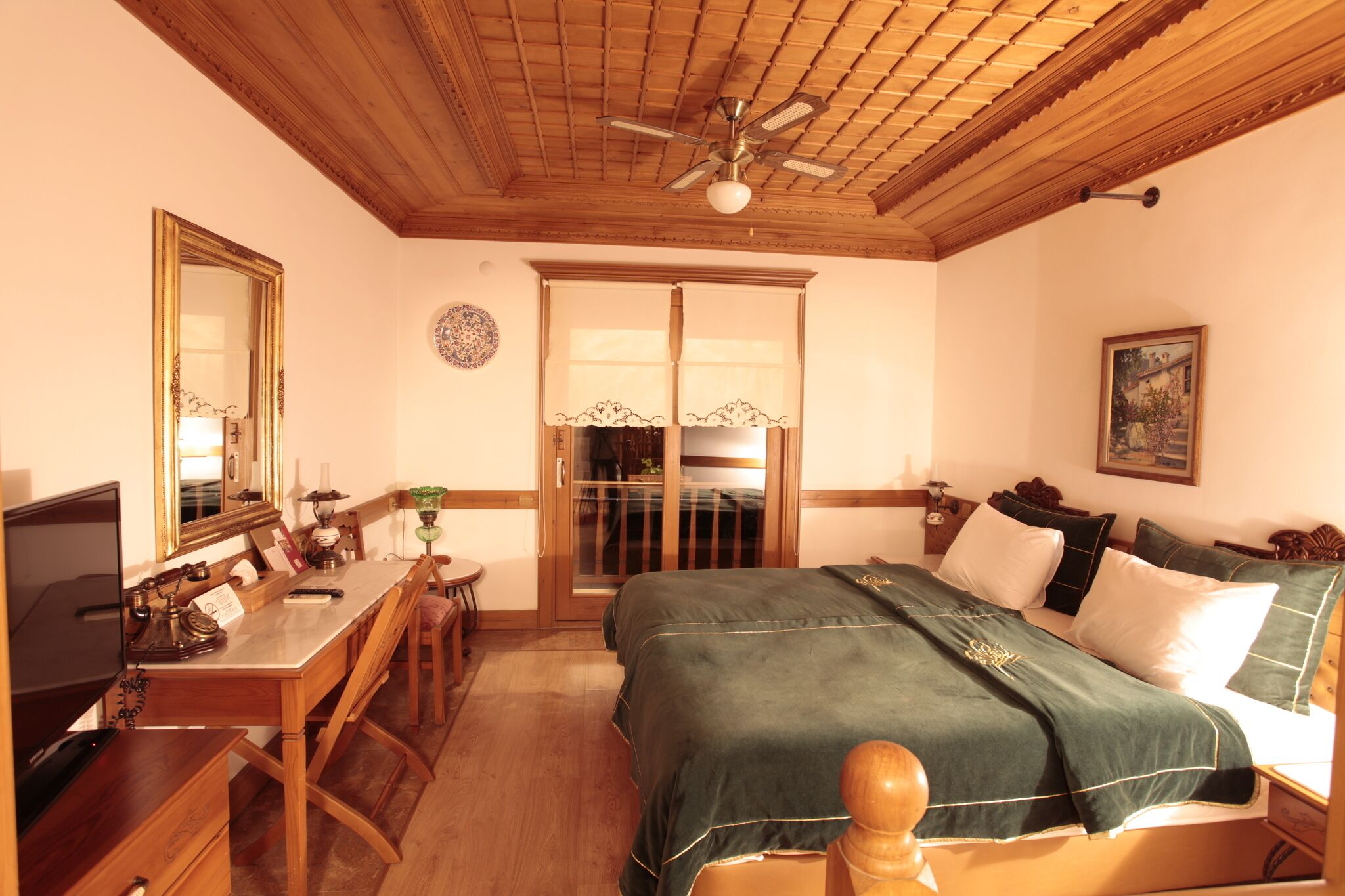 Ein Zimmer mit Bett, Schreibtisch, Stuhl, Deckenventilator und einer Tür mit Fensterteil.
