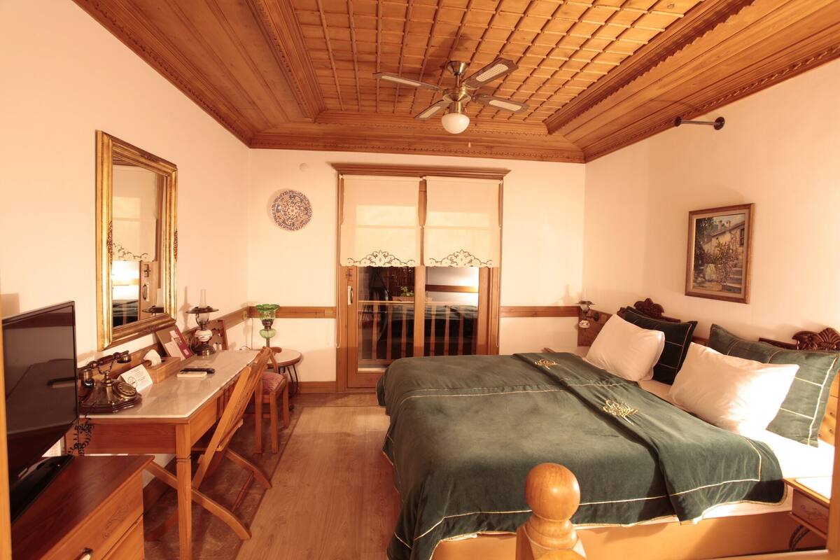A room with a bed, a desk, a chair, a ceiling fan, and a door with a glass panel.