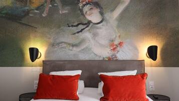 Habitación de hotel con un cuadro abstracto grande en la pared, cabecera gris, ropa de cama blanca y almohadas rojas.