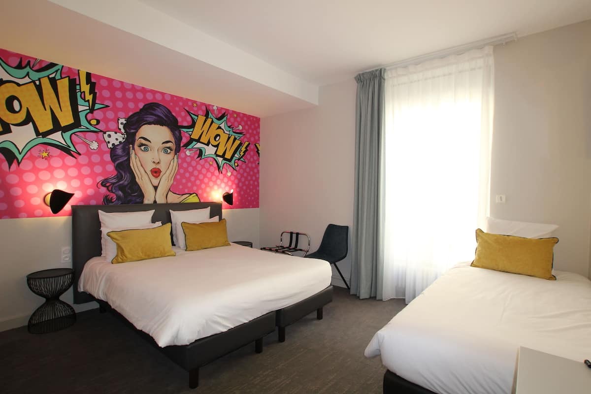 A hotel room with two beds, a large pop art mural on the wall, a desk, and a chair.