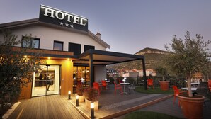 A hotel with a sign reading "HOTEL" and a covered outdoor area with tables and chairs. - Hôtel  la Capelle (Millau)
