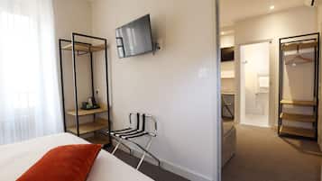 A hotel room with a bed, a TV mounted on the wall, a chair, and a walk-in closet.