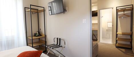 A hotel room with a bed, a TV mounted on the wall, a chair, and a walk-in closet.
