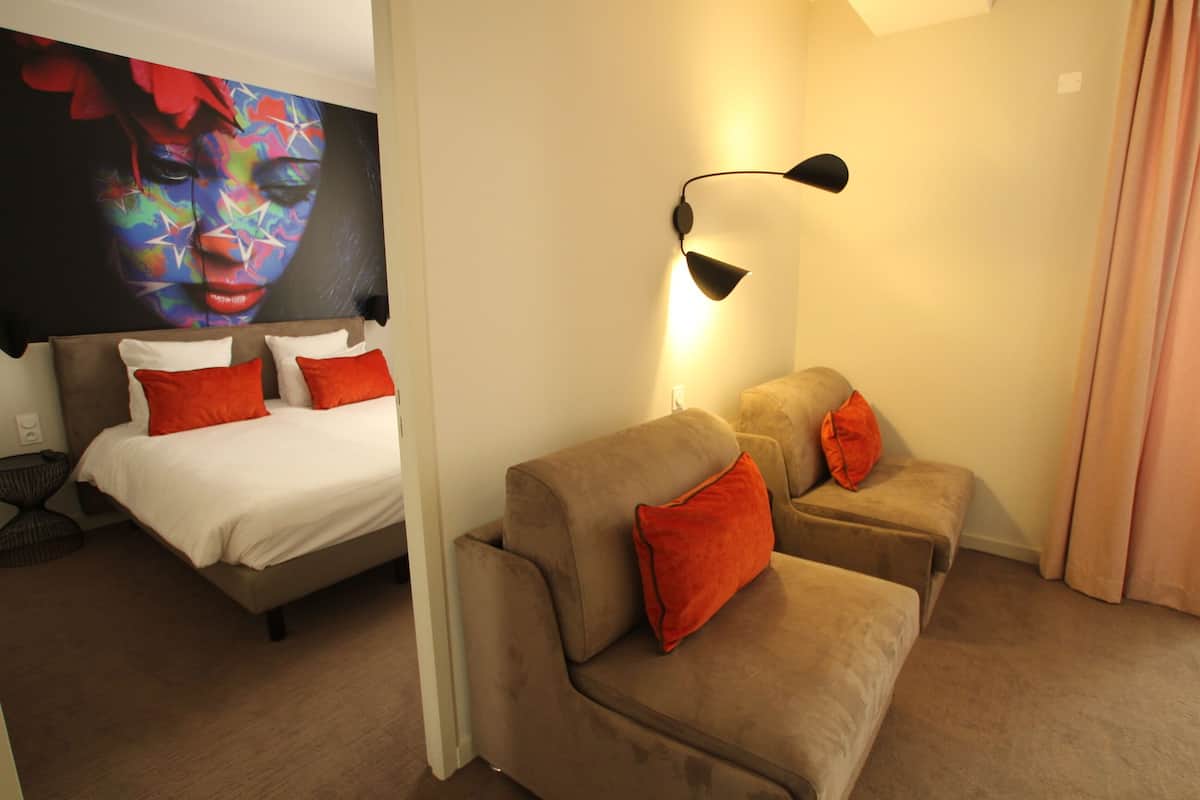 A hotel room with a bed, two sofas, a wall-mounted lamp, and a large abstract painting.