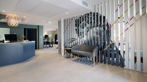 A modern reception area with a reception desk, a grey sofa, and a large abstract wall art piece. - Hôtel  la Capelle (Millau)