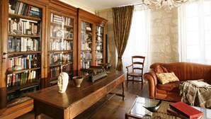 A library with wooden bookshelves, a leather sofa, and a glass coffee table. - La Porte Rouge - The Red Door Inn Chambres d'Hotes (Saintes)