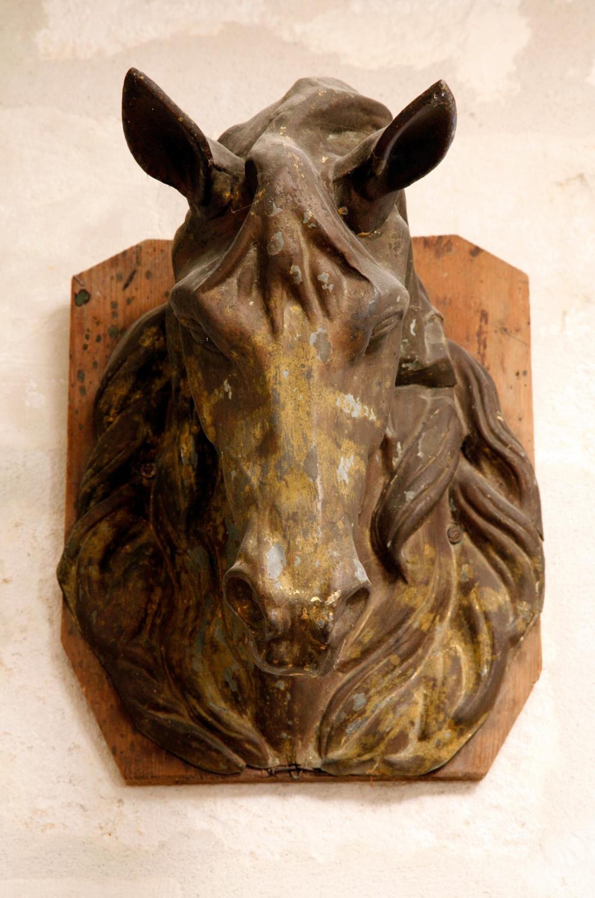 A bronze sculpture of a horse's head mounted on a wooden base.