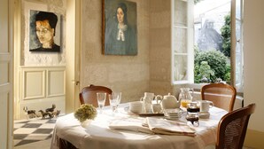 A dining area with a table set for breakfast, featuring plates, cups, and a pitcher of orange juice. There are two paintings on the wall and a window with a view of greenery outside. - La Porte Rouge - The Red Door Inn Chambres d'Hotes (Saintes)