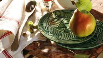 Une table avec une assiette verte, une poire, une cuillère, un couteau, un verre contenant un liquide rouge et un bol blanc.