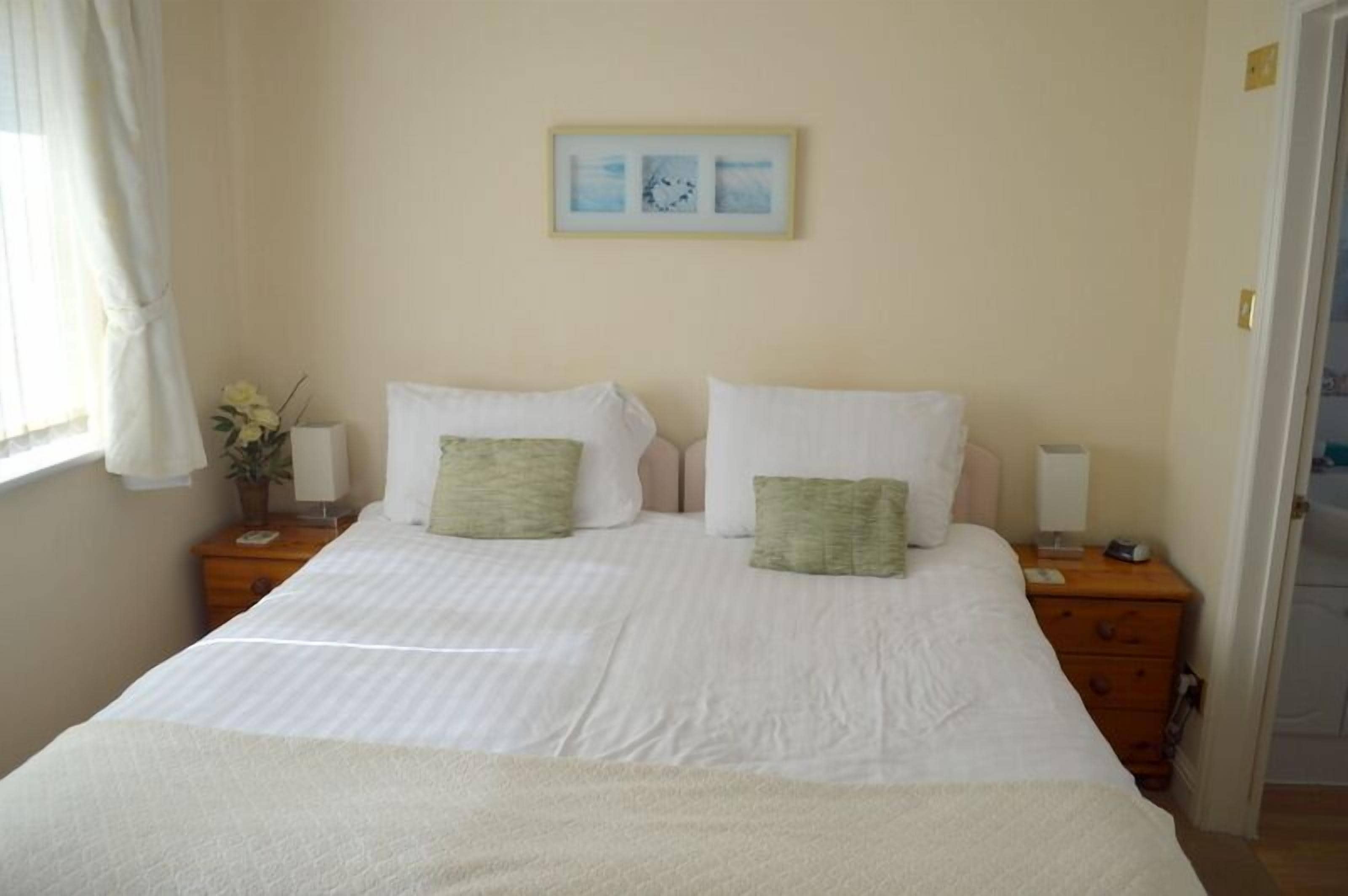 A neatly made bed with two pillows, a bedside table with a lamp, and a framed picture on the wall.