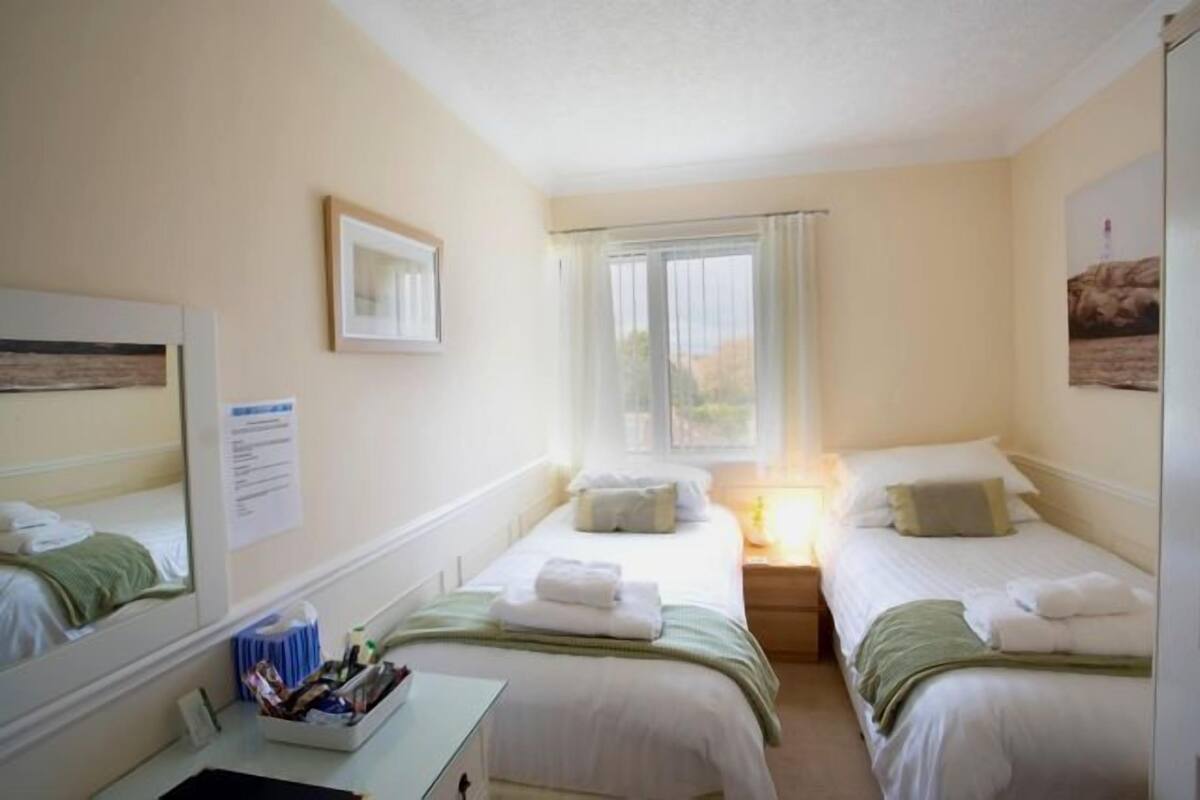 A hotel room with two beds, a desk, and a window with curtains.