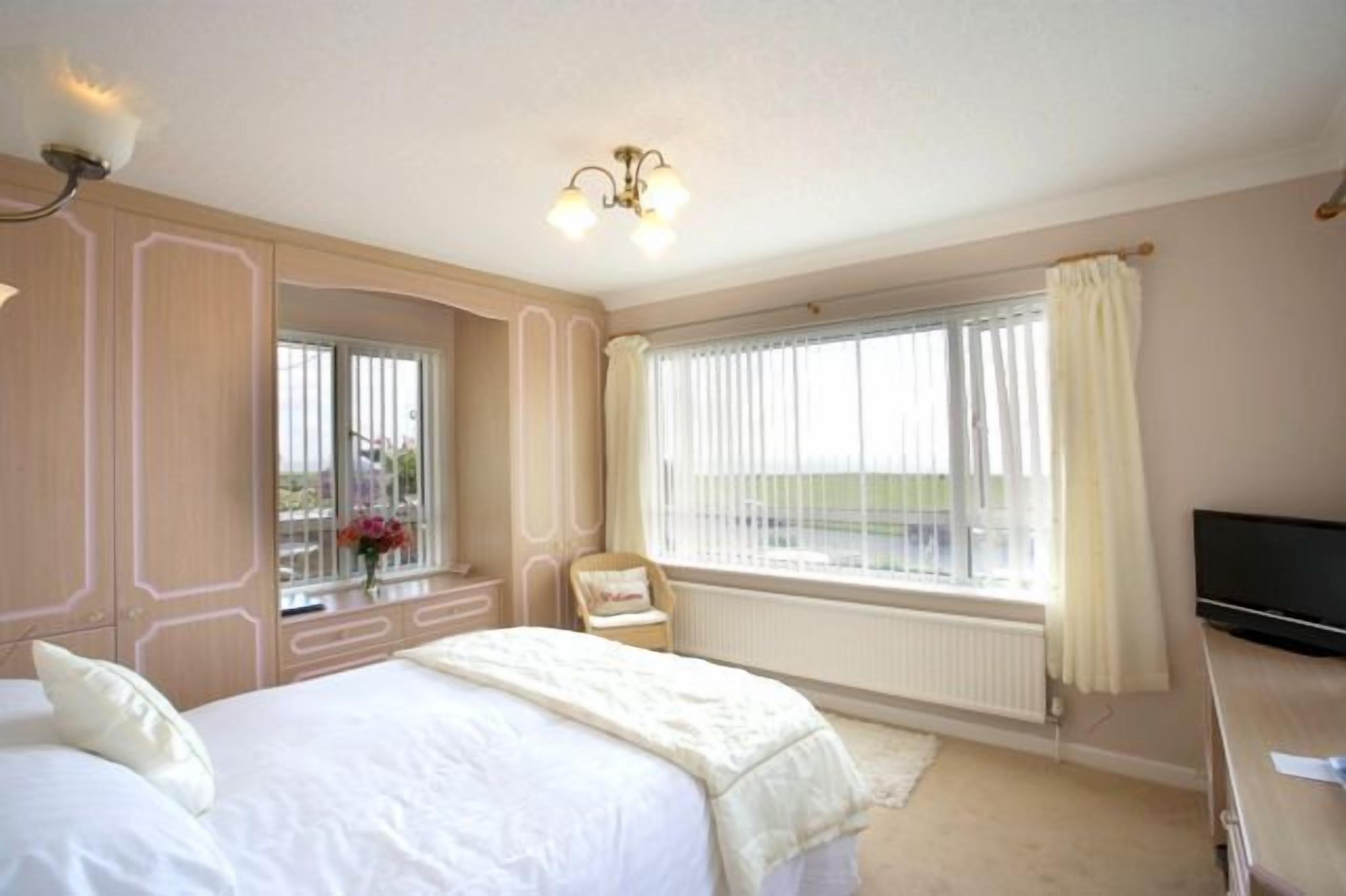 A hotel room with a large bed, a chair by the window, a TV, and a view of the outdoors.