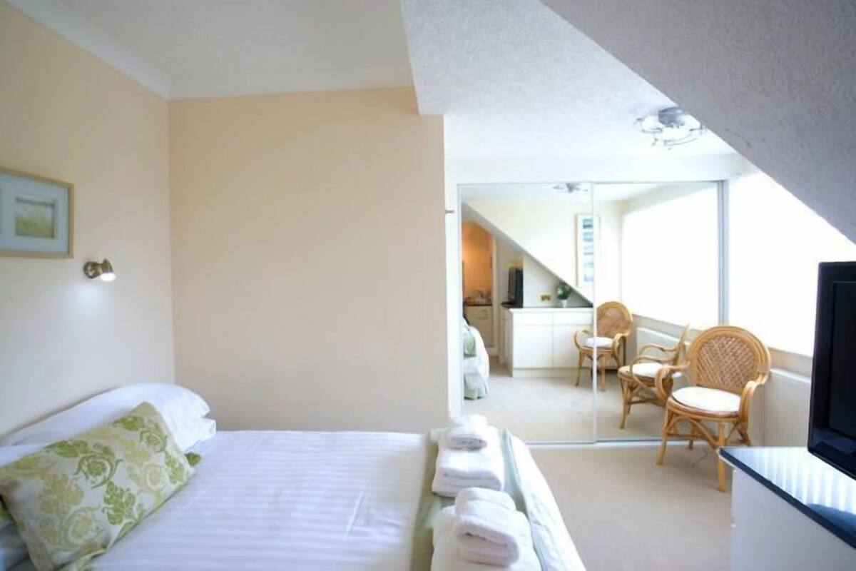 A hotel room with a bed, a chair, and a balcony with wicker furniture.