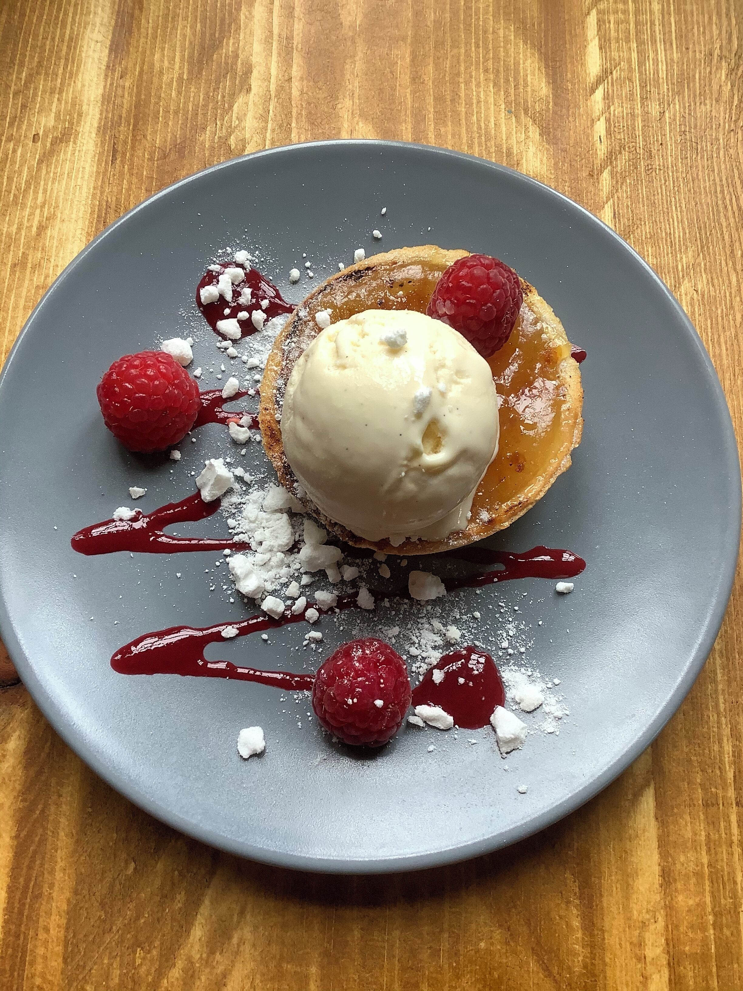 Un plato de postre con un pastel, helado, frambuesas y azúcar glas.