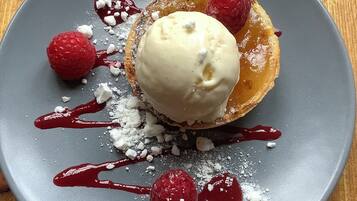 Un plato de postre con un pastel, helado, frambuesas y azúcar glas.